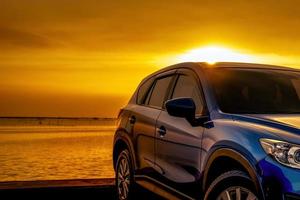 voiture suv compacte bleue au design sportif et moderne garée sur une route en béton au bord de la mer au coucher du soleil. concept de réussite commerciale. voyage en voiture. industrie automobile. technologie des voitures électriques et hybrides. photo