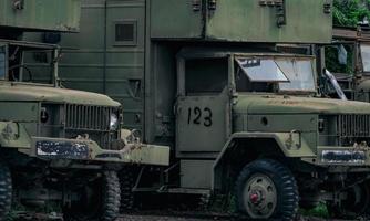 vue de face d'un vieux camion vert militaire détruit avec un vieux pneu crevé. camion militaire rouillé abandonné. camion abandonné en décomposition avec texte de l'armée américaine sur le capot. voiture pare-balles garée au parking. photo