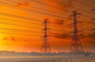 pylône électrique haute tension et fil électrique avec ciel coucher de soleil. poteaux électriques. concept de puissance et d'énergie. tour de réseau haute tension avec câble métallique. beau ciel coucher de soleil rouge-orange. Infrastructure. photo