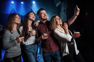 tout le monde passe un bon moment. amis prenant selfie dans une belle discothèque. avec des boissons dans les mains photo