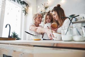 processus d'apprendre à l'enfant comment préparer la nourriture. mère, grand-mère et fille s'amusant dans la cuisine photo