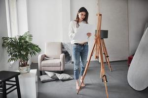 marcher dans l'atelier d'art. jeune brune dans la chambre aux murs blancs et à la lumière du jour qui vient de la fenêtre photo