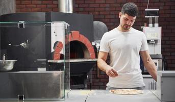 processus de travail. boulanger en chemise blanche jette des épices pour faire de délicieuses pizzas pour une commande au restaurant photo