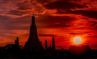 wat arun ratchawararam au coucher du soleil avec un beau ciel et des nuages rouges et orange. le temple bouddhiste wat arun est le point de repère de bangkok, en thaïlande. l'art de l'attraction. silhouette ciel dramatique et temple. photo