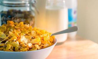 bol de céréales avec cuillère posée sur une table en bois près de granola dans un récipient en verre et un verre de lait. petit-déjeuner alimentaire de calcium pour les enfants avant d'aller à l'école le matin. concept de cornflakes et de lait photo