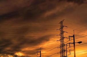 silhouette pylône électrique haute tension et fil électrique avec un ciel orange. poteaux électriques au coucher du soleil. concept de puissance et d'énergie. tour de réseau haute tension avec câble métallique à la station de distribution. photo