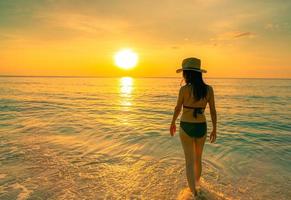 silhouette femme adulte marchant dans la mer tropicale avec un beau ciel coucher de soleil sur la plage paradisiaque. une fille heureuse porte un bikini et un chapeau de paille relaxant des vacances d'été. voyage de vacances. ambiance estivale. la vie continue. photo