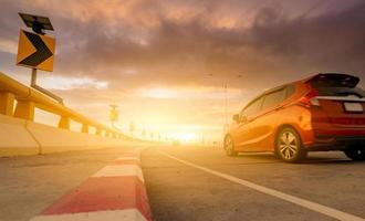 flou de mouvement d'une voiture rouge roulant sur une route en béton courbe avec un panneau de signalisation. voyage sur la route pendant les vacances d'été. conduite en voiture dans la rue. voyage d'été en voiture. énergie solaire sur panneau de signalisation courbe jaune photo