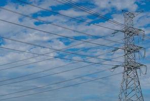 pylône électrique haute tension et fil électrique contre le ciel bleu et les nuages. vue de dessous du pylône électrique. tour de réseau haute tension avec câble métallique. lignes de transmission sur la tour du réseau haute tension. photo