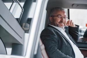 se sent satisfait. homme d'affaires heureux dans des verres assis dans la nouvelle voiture de luxe photo