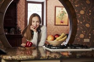 faire une pause. jolie jeune femme debout dans la cuisine moderne près de la cuisinière à gaz photo