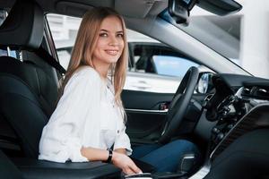 regarde droit dans la caméra. belle fille blonde assise dans la nouvelle voiture avec un intérieur noir moderne photo