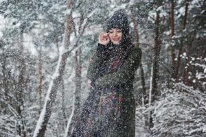 c'est une belle chute de neige. joyeuse jeune fille dans des vêtements chauds se promener dans la forêt d'hiver pendant la journée photo