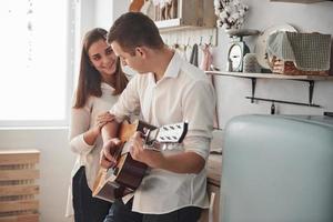 homme gagnant la femme. jeune guitariste jouant une chanson d'amour pour sa petite amie dans la cuisine photo