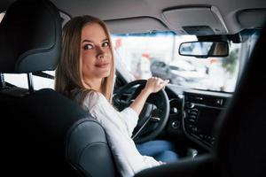 maintenant on fait demi-tour. belle fille blonde assise dans la nouvelle voiture avec un intérieur noir moderne photo