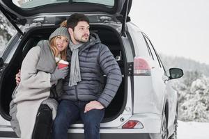 Calin chaleureux. un beau couple passe un week-end à la campagne en hiver. assis sur la partie arrière d'une voiture moderne photo