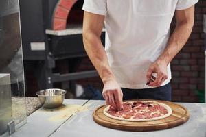 faire son travail. boulanger en chemise blanche mettant des olives pour faire de délicieuses pizzas pour une commande au restaurant photo
