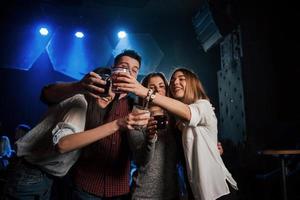 vue de face. groupe de jeunes amis souriant et portant un toast dans la discothèque photo