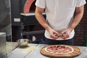 faire un produit délicieux. boulanger en chemise blanche mettant des olives pour faire de délicieuses pizzas pour une commande au restaurant