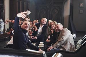 vue de face d'un gars prenant un selfie de groupe. amis de la famille s'amusant dans un beau restaurant moderne de luxe photo