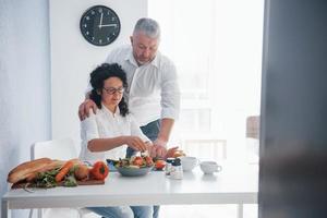 bravo, on peut le manger. homme et sa femme en chemise blanche préparant de la nourriture dans la cuisine à l'aide de légumes photo