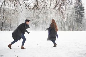 courir dans le parc. magnifique jeune couple jouant et lançant des boules de neige dans la forêt d'hiver photo