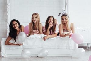 ballons blancs et roses. filles joyeuses en vêtements de nuit allongées sur le lit dans une salle blanche et célébrant photo