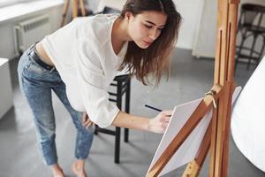 c'est comme ça que les dessins sont faits. jeune brune dans la chambre aux murs blancs et à la lumière du jour qui vient de la fenêtre photo