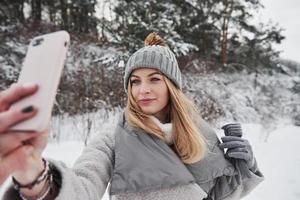 femme prenant selfie à l'extérieur près de la forêt au jour d'hiver enneigé photo