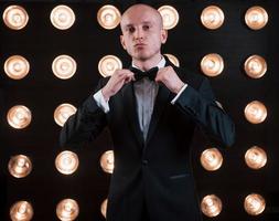 ajuste la cravate. prêt pour le spectacle. magicien en costume noir debout dans la salle avec un éclairage spécial dans les coulisses photo