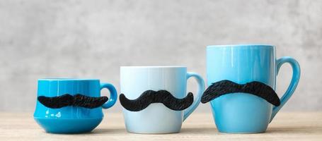 tasse à café bleue et tasse à thé avec décor de moustache noire sur fond de table en bois le matin. novembre bleu, bonne fête des pères et concept de journée internationale des hommes photo