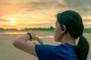 une femme asiatique porte dans l'oreille de vrais écouteurs sans fil touchant une bande intelligente après avoir couru le matin. ordinateur portable. bracelet cardiofréquencemètre. appareil de remise en forme. appareil connecté à une montre intelligente. photo