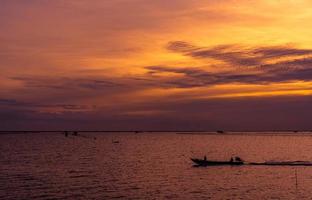 beau ciel coucher de soleil dramatique. ciel et nuages de coucher de soleil sombre et orange. fond de nature pour un concept tranquille et paisible. mer tropicale au crépuscule. bateau à longue queue naviguant par un pêcheur. beauté dans la nature. photo