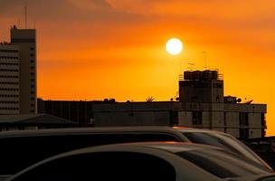 ville et embouteillage le soir avec un beau ciel orange au coucher du soleil. immeuble résidentiel en béton en zone urbaine. transport de silhouette sur embouteillage près de l'appartement. voiture floue conduite sur la route.