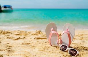 sandales roses et blanches, lunettes de soleil sur la plage de sable au bord de la mer. flipflop et lunettes de style mode décontracté au bord de la mer. vacances d'été sur la plage tropicale. voyage de vacances amusant sur la plage de sable. heure d'été. photo