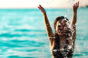 heureuse jeune femme asiatique en maillot de bain noir se détendre et profiter de vacances à la plage paradisiaque tropicale. fille en vacances d'été éclabousser l'eau dans la mer. modèle sexy. femme sexy en bikini noir. ambiance estivale. photo