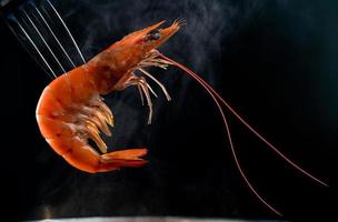 crevettes cuites à la vapeur sur fourche isolées sur fond sombre avec espace de copie. buffet de fruits de mer dans le concept de restaurant. utiliser pour la publicité des promotions de buffet de fruits de mer photo