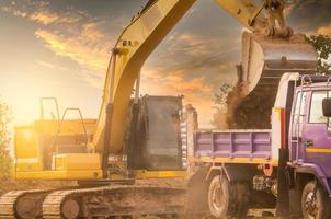 rétrocaveuse travaillant en creusant le sol sur le chantier de construction et en chargeant dans le camion. seau de terre de transport de rétrocaveuse au camion. la pelle sur chenilles décharge le sol de terre dans un camion à benne basculante lourd. engin d'excavation. photo