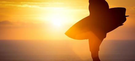 surfeur debout avec sa planche de surf sur la plage au coucher du soleil sur l'océan photo