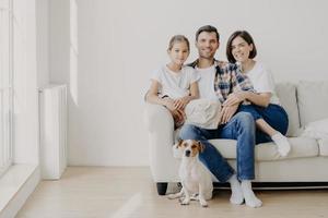 vue horizontale de trois membres sympathiques de la famille et d'un petit chien de race pose à l'appareil photo pour faire des photos mémorables. dauther passe du temps libre avec sa mère et son père, bonne journée à la maison