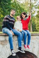 femme reposante insouciante, homme et petite fille mignonne assis sur le pont à l'extérieur, admirer le lever du soleil. mère affectueuse montre à sa petite fille la beauté de la nature. la famille aime passer du temps libre dans le parc photo