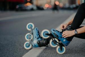 les jambes d'une femme méconnaissable mettent des patins à roulettes qui vont faire des exercices en plein air mène un style de vie actif pose sur la route de la rue se prépare pour le patinage en ligne. patineur sans visage se lance dans un sport dangereux photo