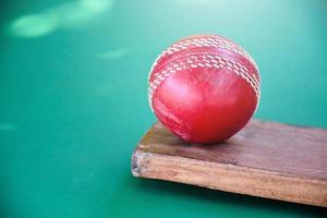 gros plan sur de vieux équipements de sport de cricket sur un sol vert, une vieille balle en cuir, une batte en bois, une mise au point douce et sélective, des amateurs de sport de cricket traditionnels dans le monde entier. photo