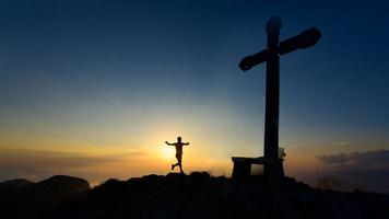 le coureur de montagne arrive au sommet où il y a une croix au coucher du soleil photo