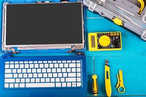 l'assistant répare l'ordinateur portable avec des outils et des mains sur la table en bois bleue. vue de dessus photo