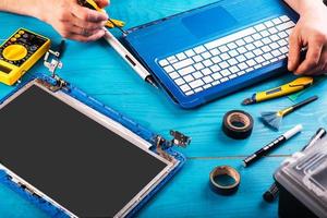 l'assistant répare l'ordinateur portable avec des outils et des mains sur la table en bois bleue. vue de dessus photo