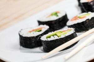 sushi au saumon, avocat, riz aux algues et baguettes sur une assiette.