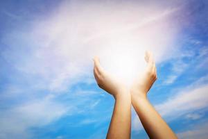 mains levées attrapant le soleil sur le ciel bleu. concept de spiritualité, bien-être, énergie positive photo