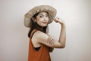 magnifique jeune femme asiatique forte avec une robe orange et un chapeau de paille montrant des biceps et souriant. concept fort de fille indonésienne. photo