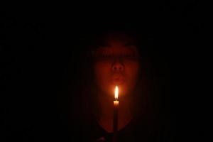 femme asiatique soufflant une bougie dans la nuit noire photo